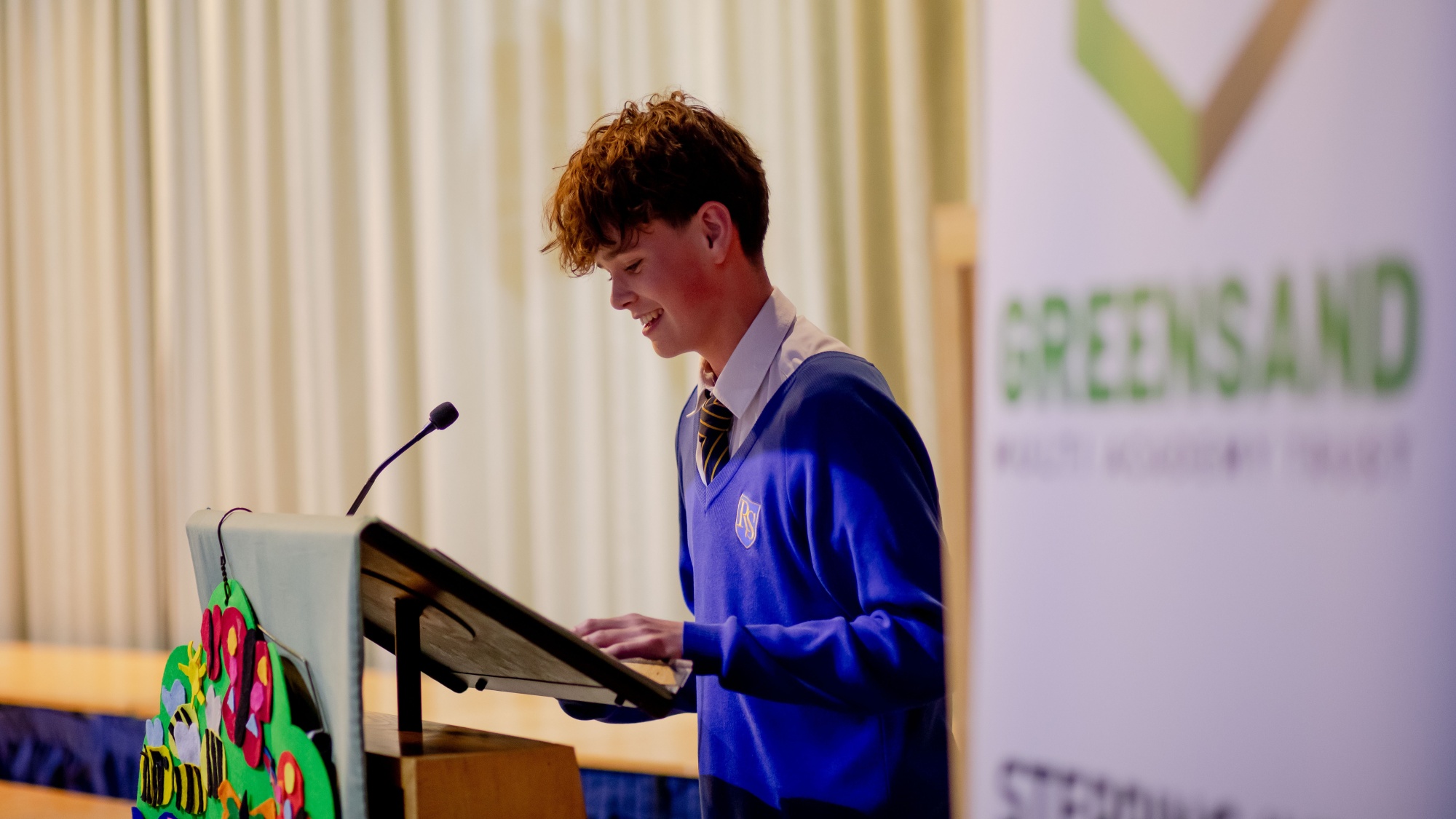 A student from Reigate College reading in front of a Greensand banner.