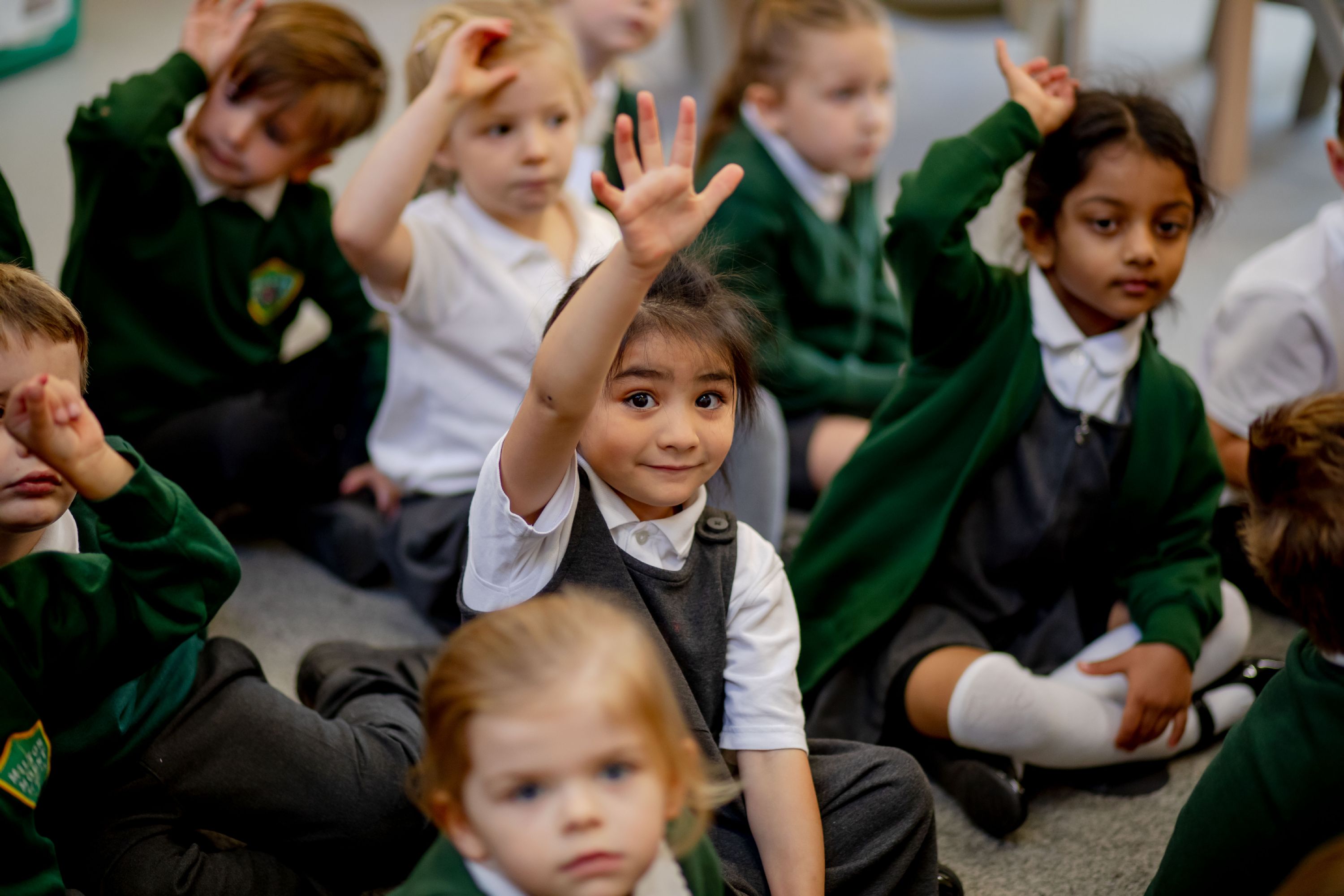 Children from Milton Mount sat on the carpet with their hands up to answer a question
